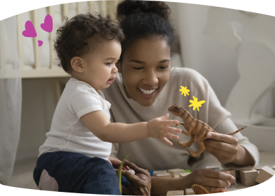 Uma babá sorridente segura um dinossauro de brinquedo para um bebê curioso, sentados juntos no chão rodeados de blocos de madeira e outros dinossauros.